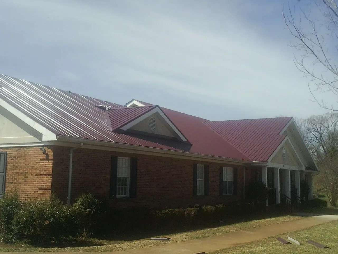 Red metal roof with gabled entries on a long brick building, from a Hail Damage Roof Repair job in Madison Heights