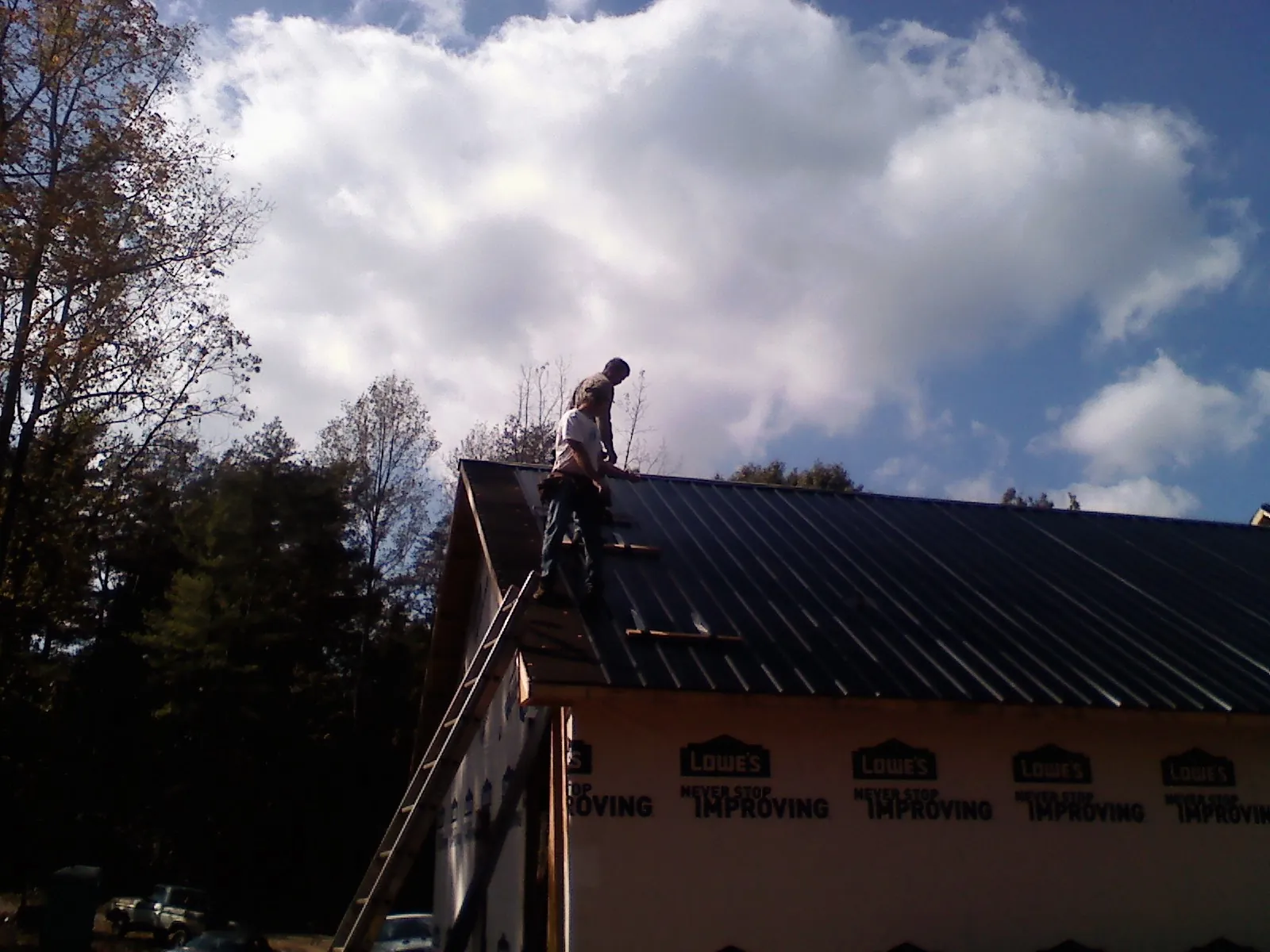 Roofer fastening dark metal panels high against a cloudy sky, from a Roof Inspection job in Madison Heights