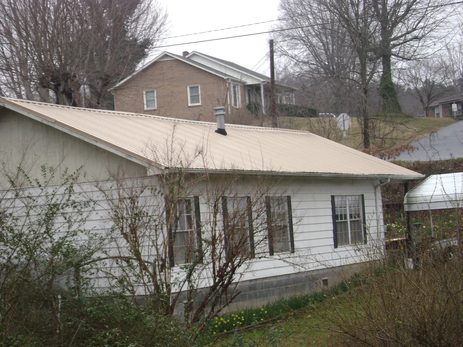 Tan metal roof on a white sided house set into a hillside — Commercial Roofing by Roofing Brothers in Madison Heights