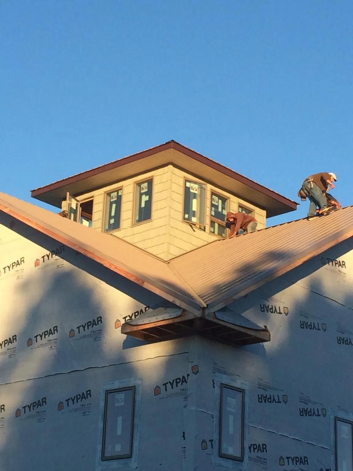 Roofers working around a rooftop cupola on a new metal roof at sunset — Roof Waterproofing in Madison Heights by Roofing Brothers